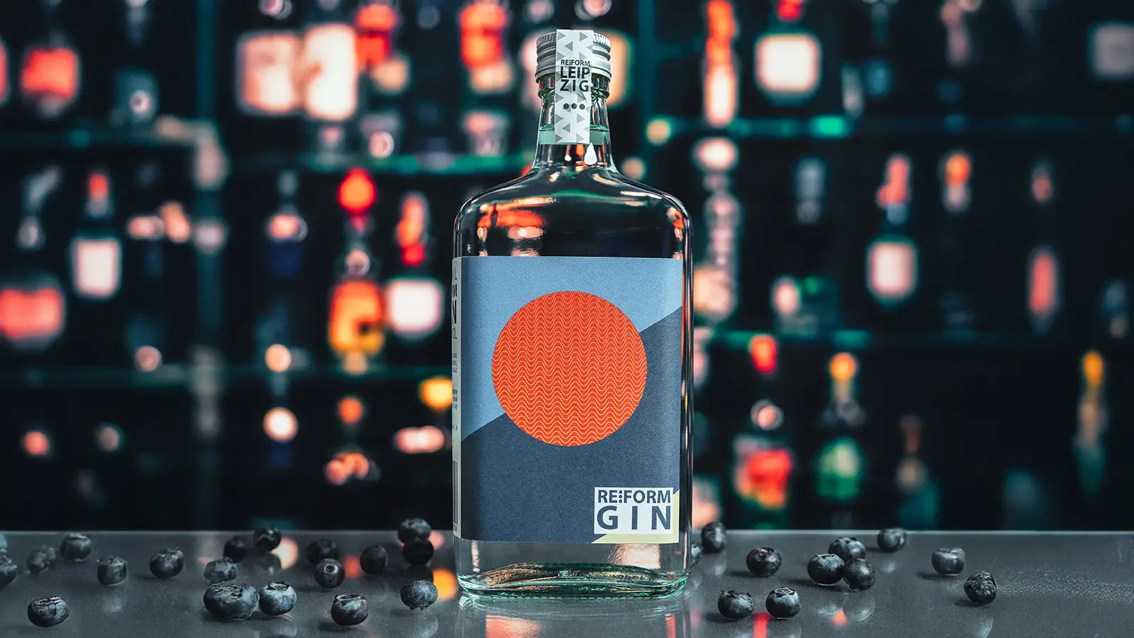Reform Gin auf spiegelndem Tisch mit Heidelbeeren und angedeuteter Bar im Hintergrund as Moodbild